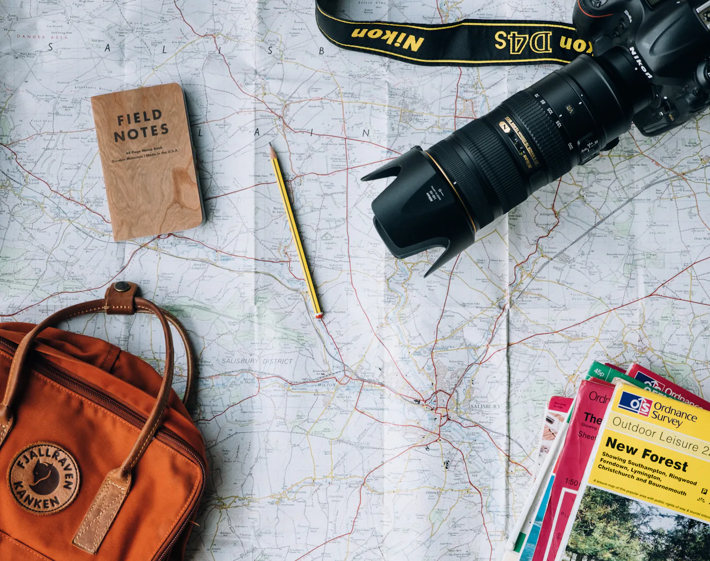 A map spread out with a camera, notebook, pencil and backpack on top