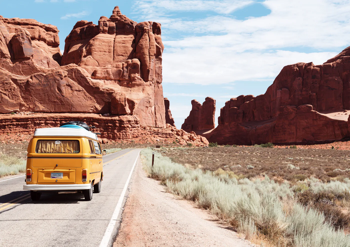 A yellow camper van on an open road winding through red rock country