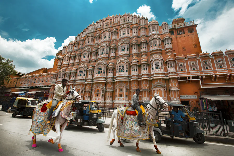 The pink facade of Hawa Mahal in Jaipur with decorated horses passing by
